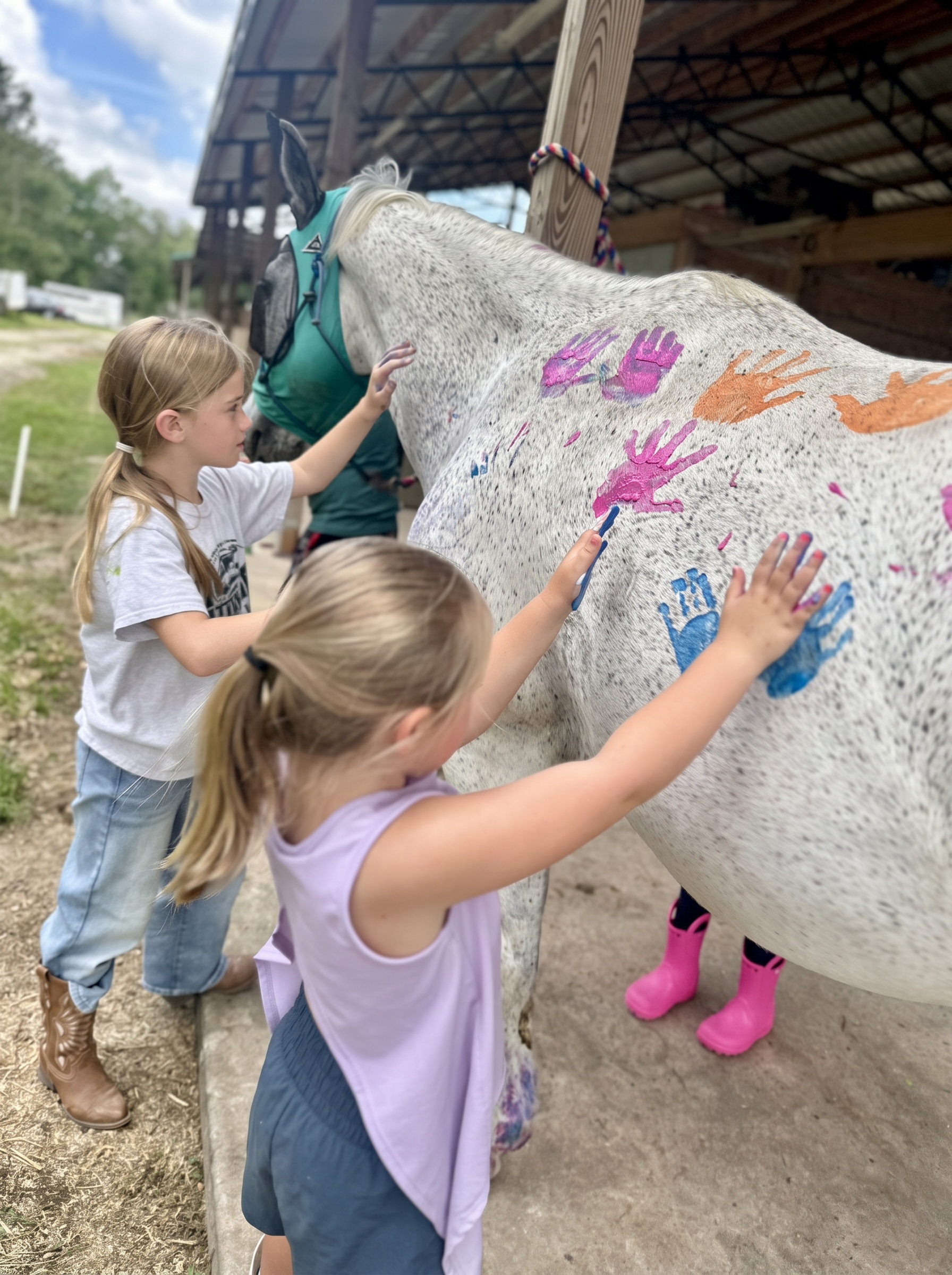 Two girls pressing painted handprints onto a white horse at a birthday party